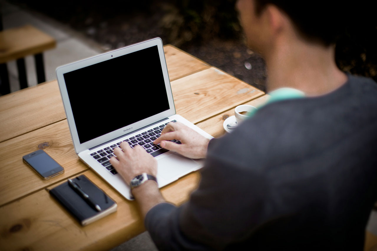 A man works on a laptop with a notebook and pen - Photo by Alejandro Escamilla on Unsplash